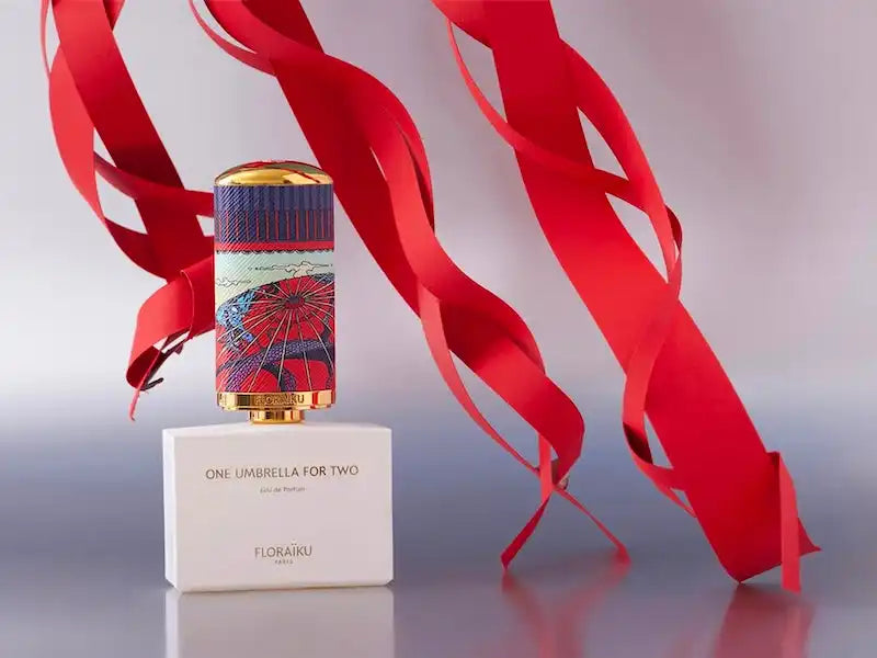 A perfume bottle with decorative red ribbons flowing around it.